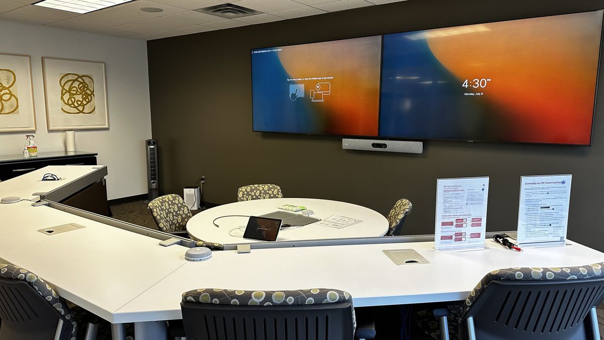 Collaboration room with dual wall displays, a video bar, U-shaped tables, and a round center table, by Enlightened Audiovisual