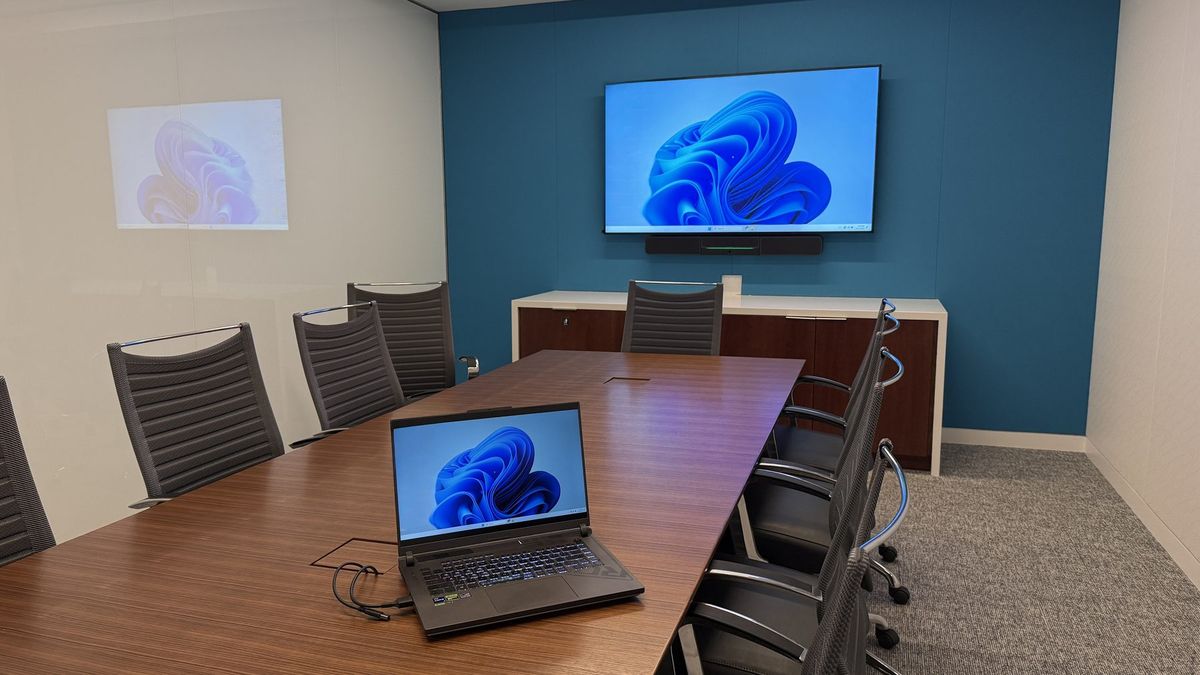 Conference room with a blue accent wall, wall display with video bar, and a long boardroom table, by Enlightened Audiovisual