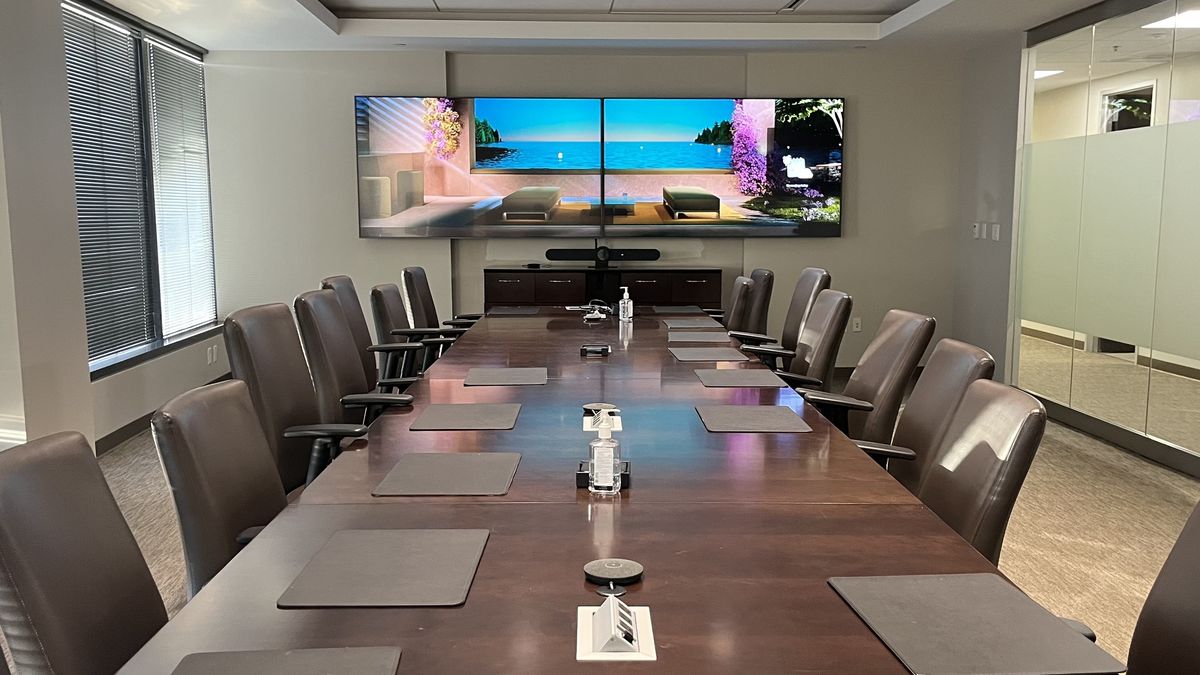 Executive boardroom with dual wall displays, a video bar, and a long wood conference table, by Enlightened Audiovisual