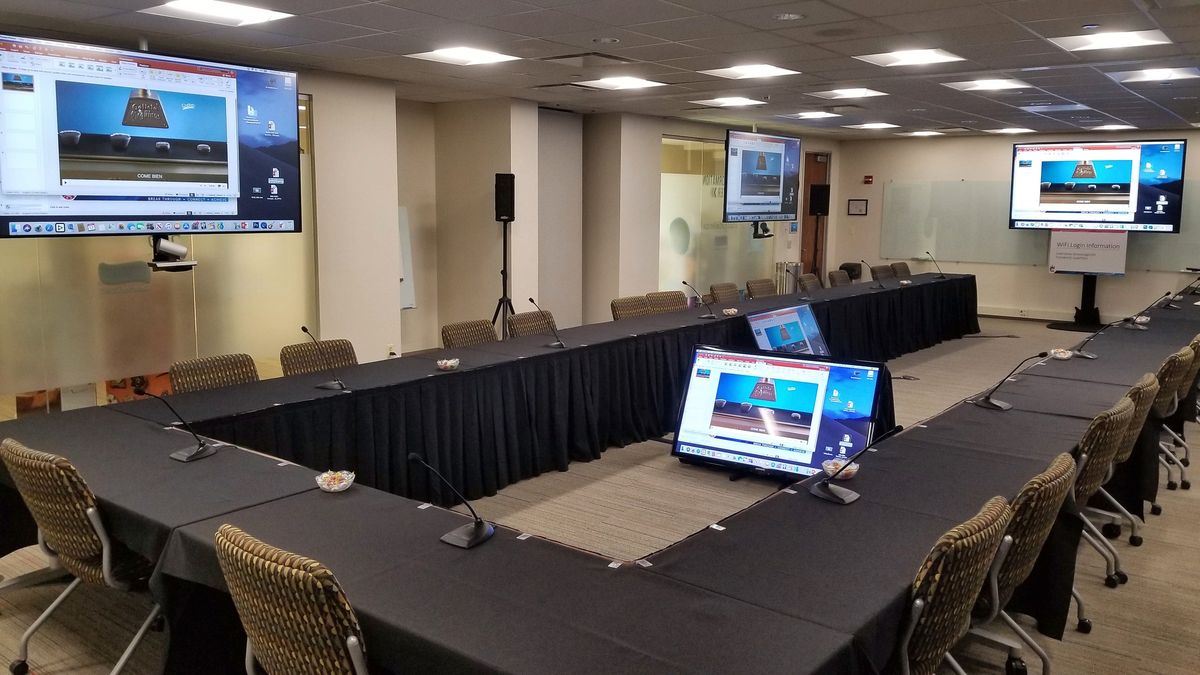 Hollow-square meeting room with gooseneck microphones at every seat and displays on every wall, by Enlightened Audiovisual