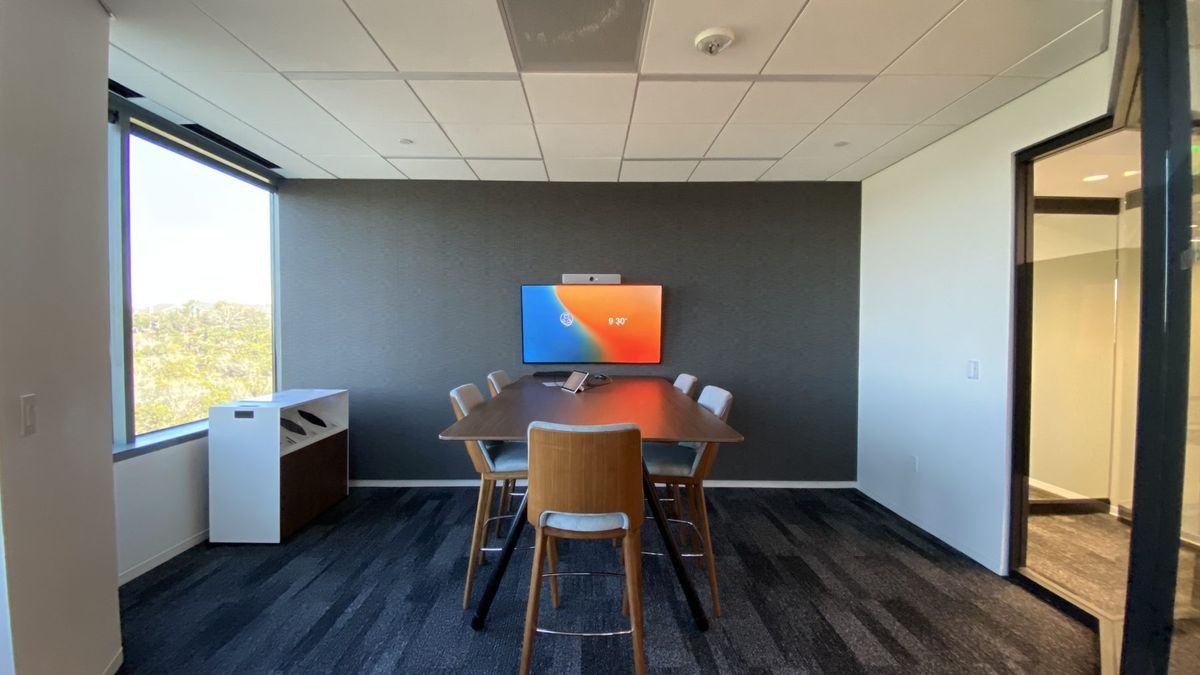 Huddle room with a window, a wall display and camera, and a tabletop touch panel, by Enlightened Audiovisual