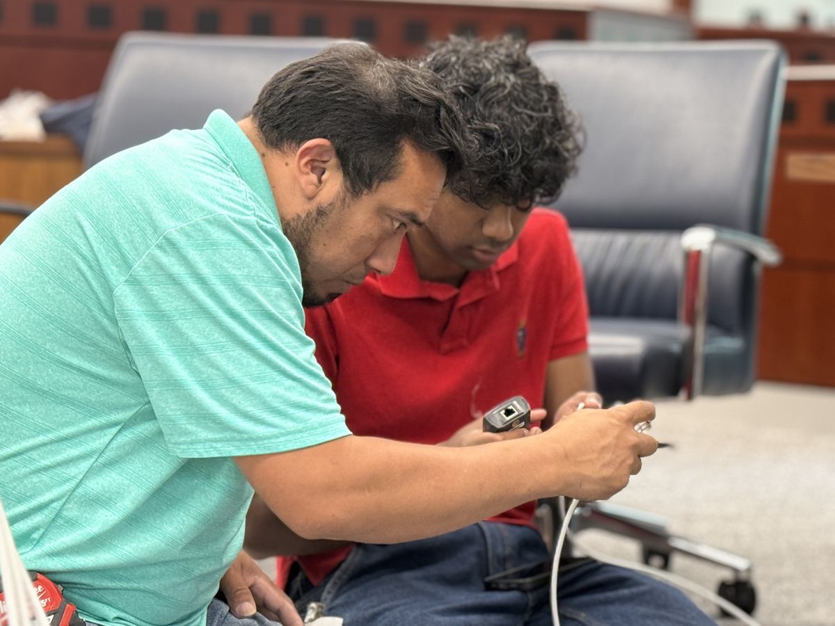 Two technicians terminating and testing a cable in a boardroom, by Enlightened Audiovisual