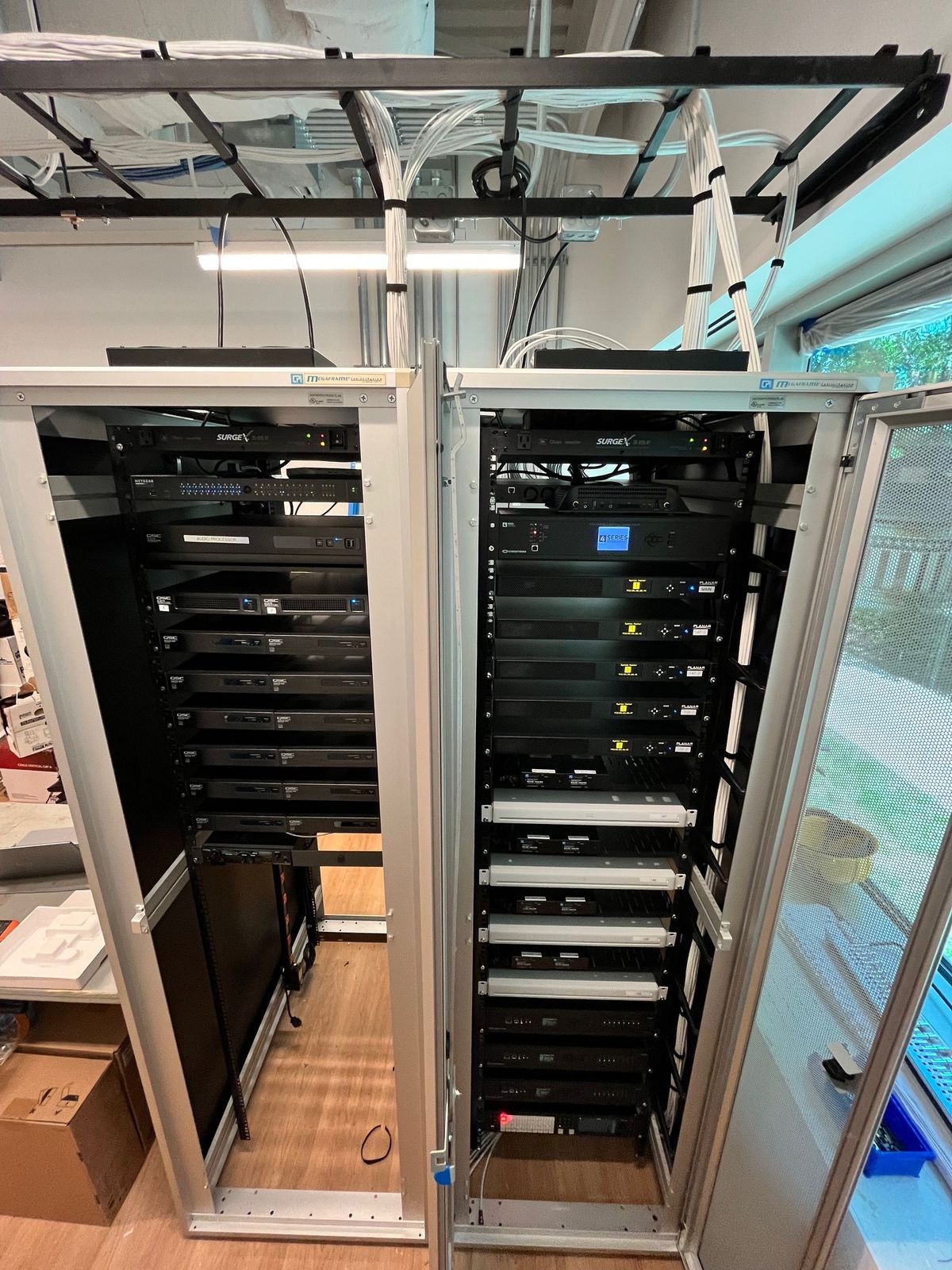 Twin open equipment racks with installed AV gear and an overhead cable tray, by Enlightened Audiovisual
